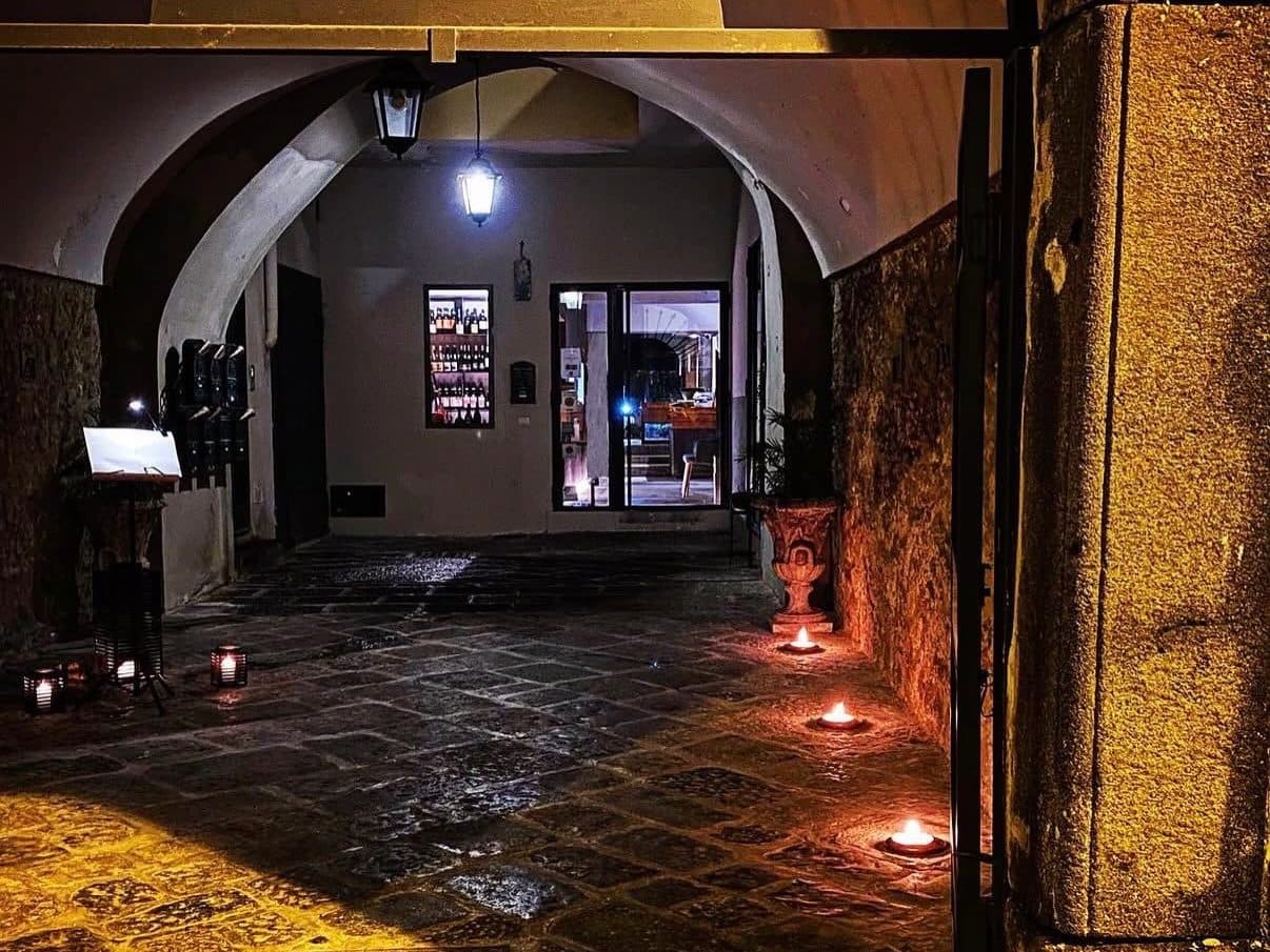 L'androne di Hydra a sera, con le candele accese sul selciato e la vetrina illuminata in fondo