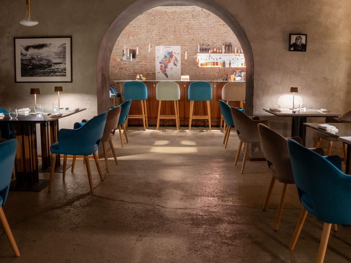 La stessa sala oggi: l'arco in pietra apre sul bancone, con le poltroncine di velluto e le lampade sui tavoli